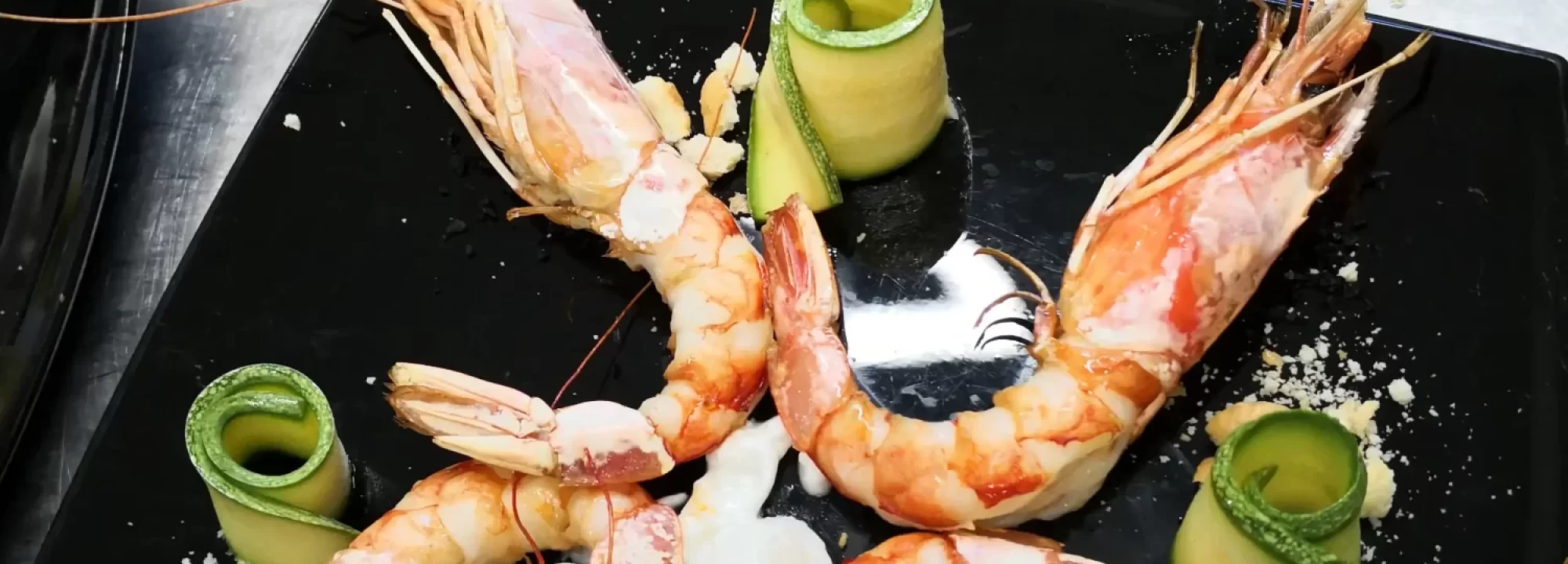 Piatto elegante di gamberi e zucchine su piatto nero guarnito con crema bianca.