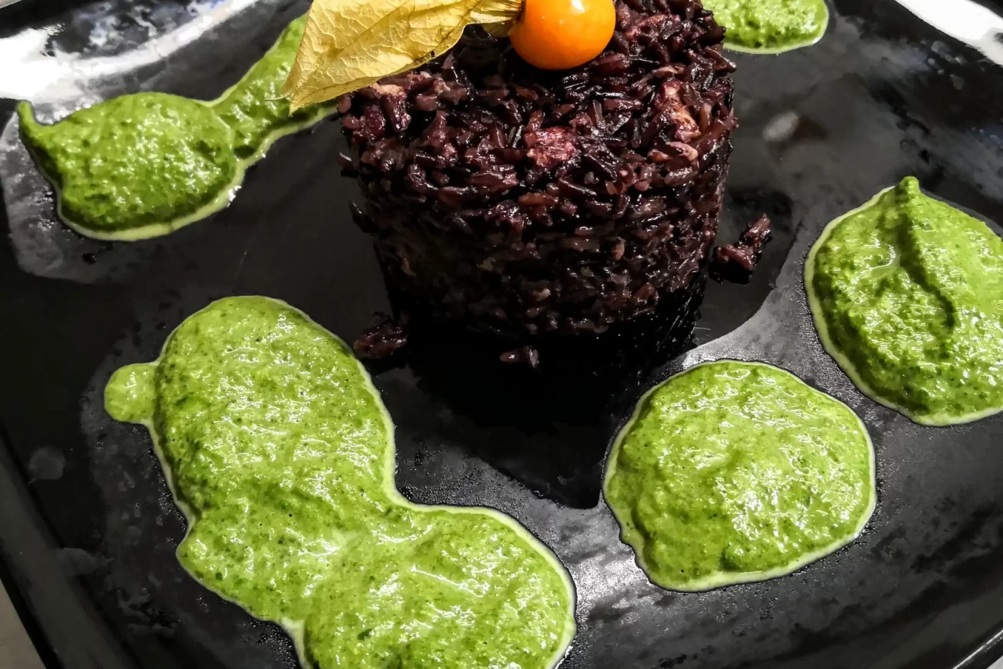 Piatto di riso nero con crema di verdure e decorazione di physalis su piatto nero.