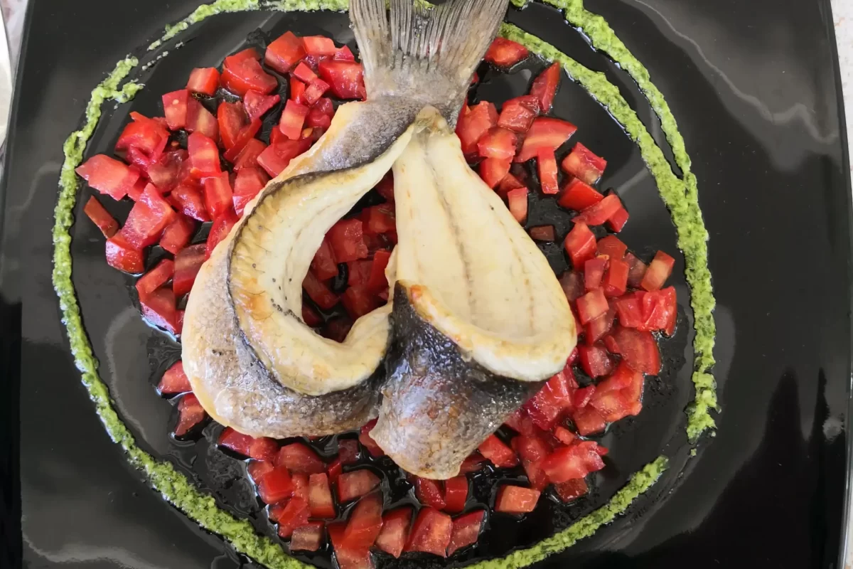 Un elegante piatto di pesce con il corpo disposto a cerchio su una salsa verde e guarnito con cubetti di pomodoro.