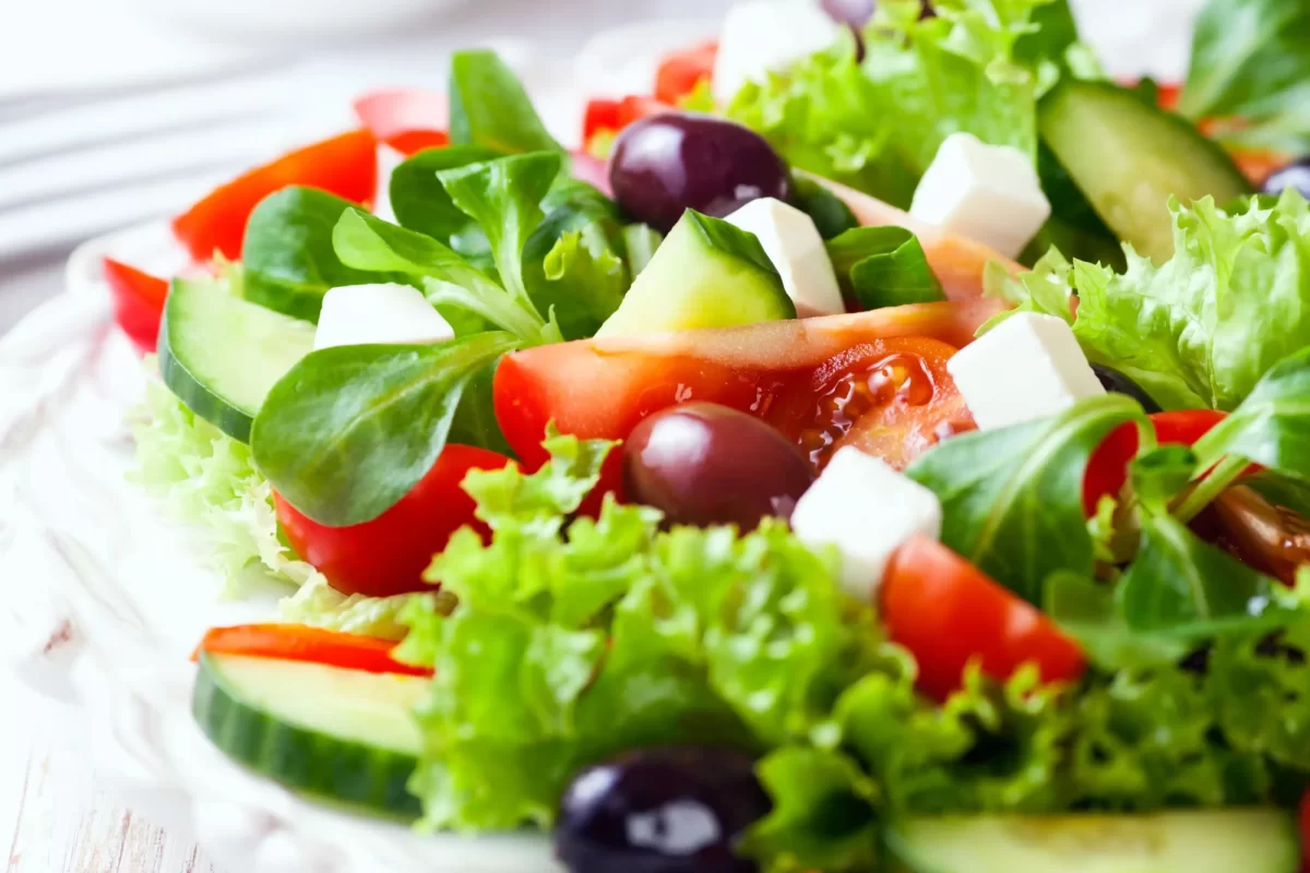 Insalata fresca con lattuga, pomodori, cetrioli, olive e feta su un piatto bianco.
