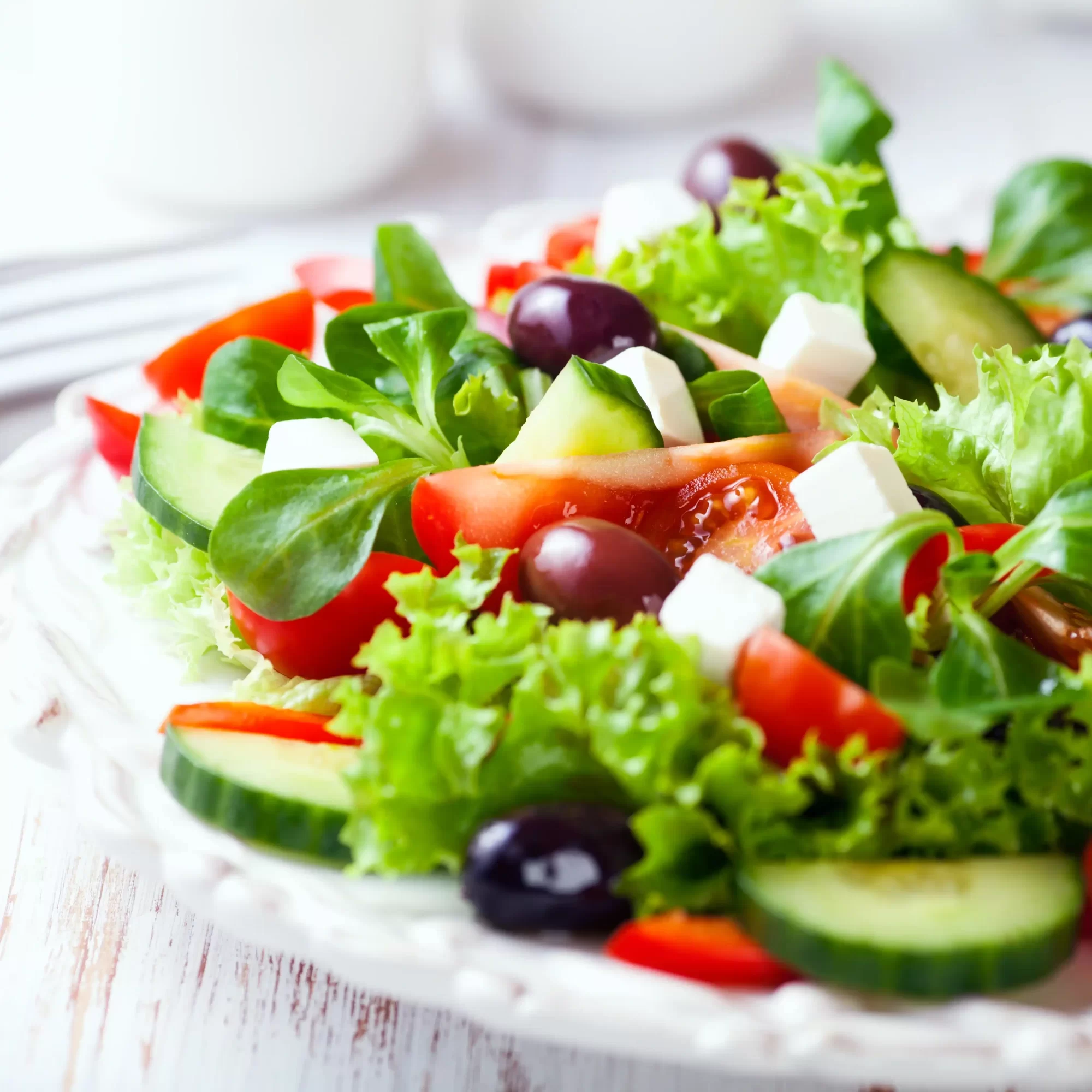 Insalata fresca con lattuga, pomodori, cetrioli, olive e feta su un piatto bianco.