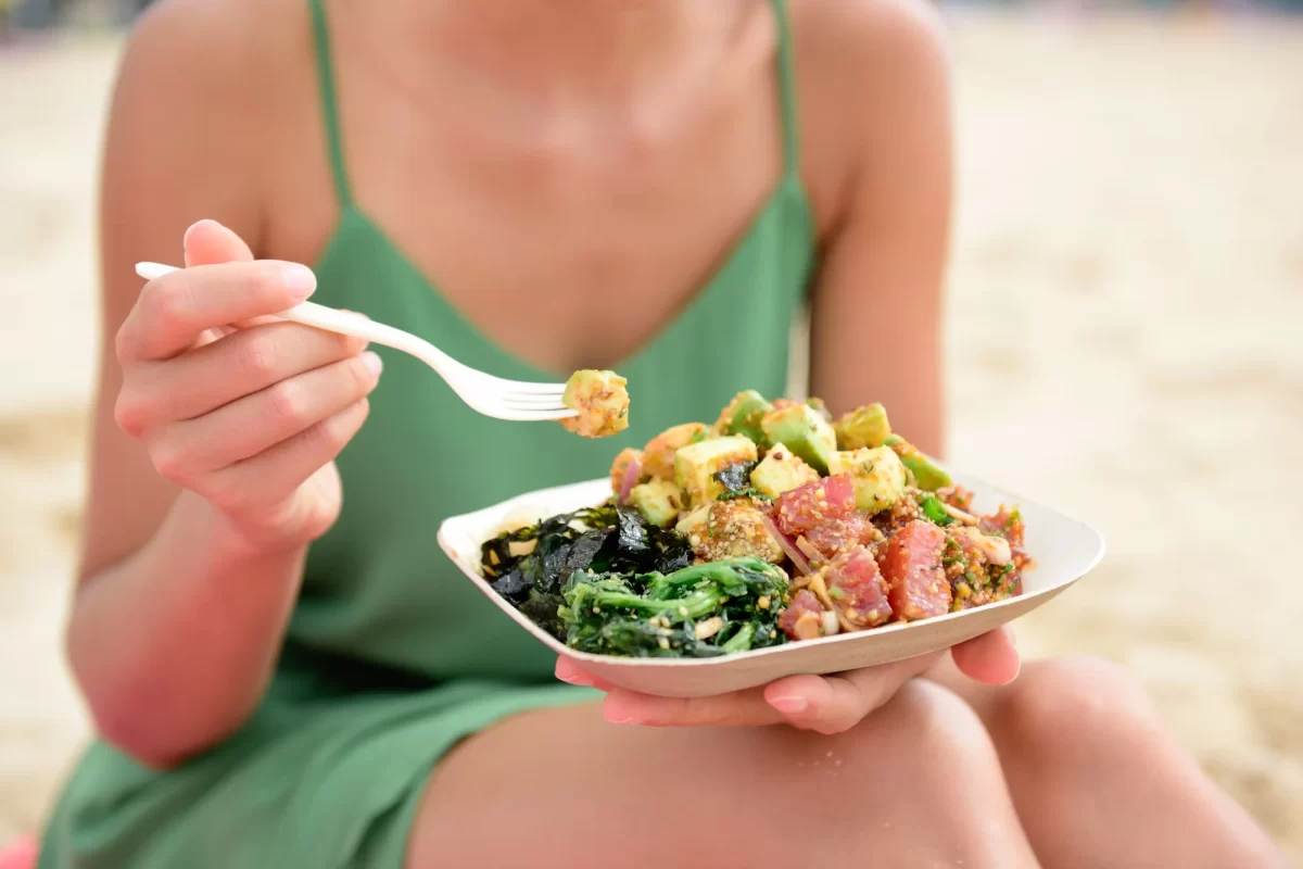 Persona che mangia una poke bowl sulla spiaggia.