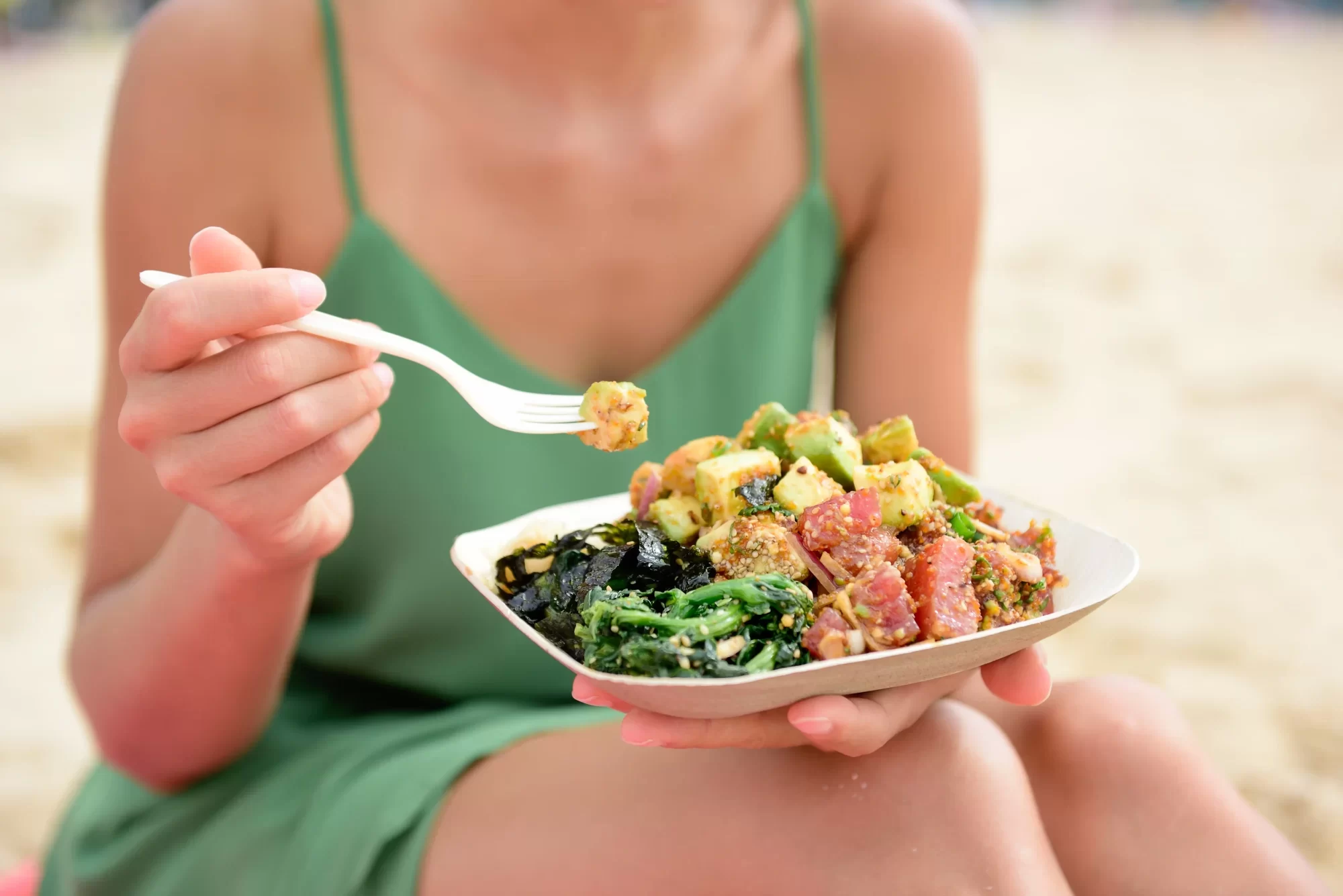 Persona che mangia una poke bowl sulla spiaggia.