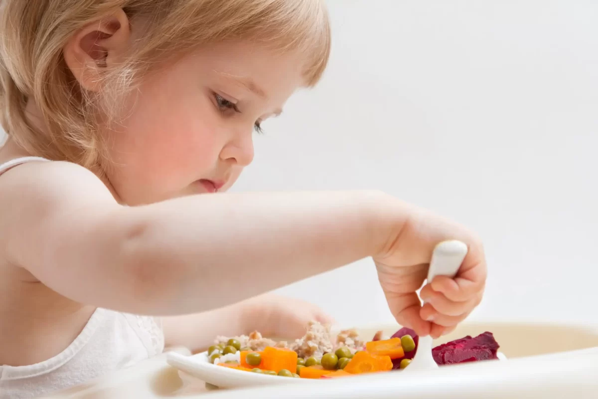 Bambina che mangia verdure con una forchetta.