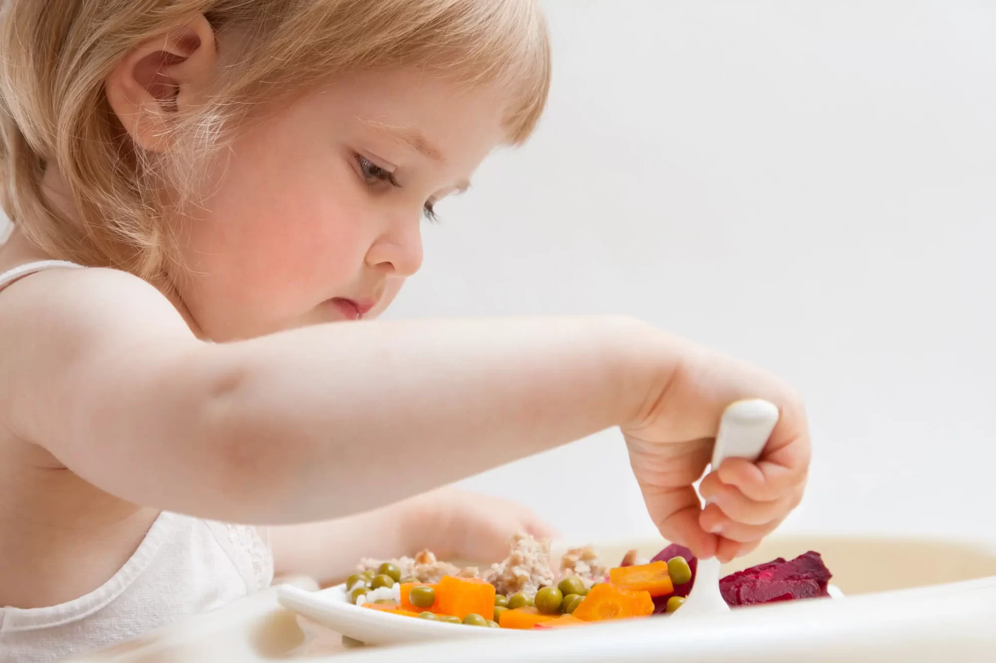Bambina che mangia verdure con una forchetta.