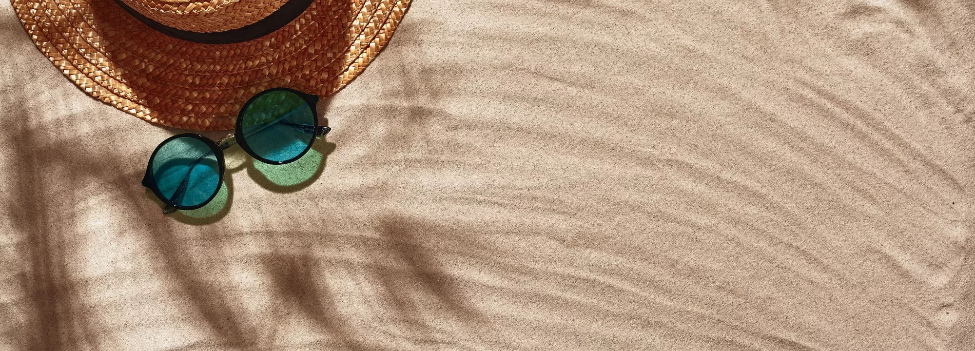 Cappello di paglia e occhiali da sole blu sulla sabbia.