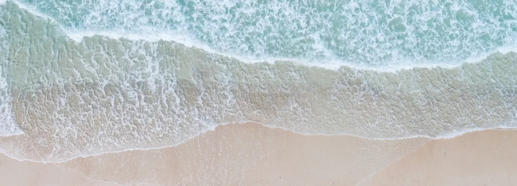 Vista aerea di onde che si infrangono su una spiaggia sabbiosa.